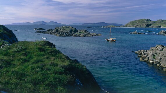 Rocky inlet with an anchored boat and hills in Rùm