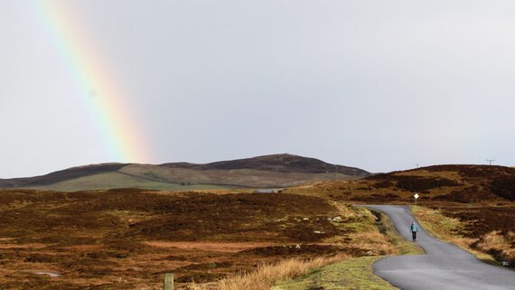 A rainbow over moorland and a single-track road in Shetland