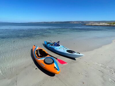 Two kayaks pulled up on a white sand beach beside clear water